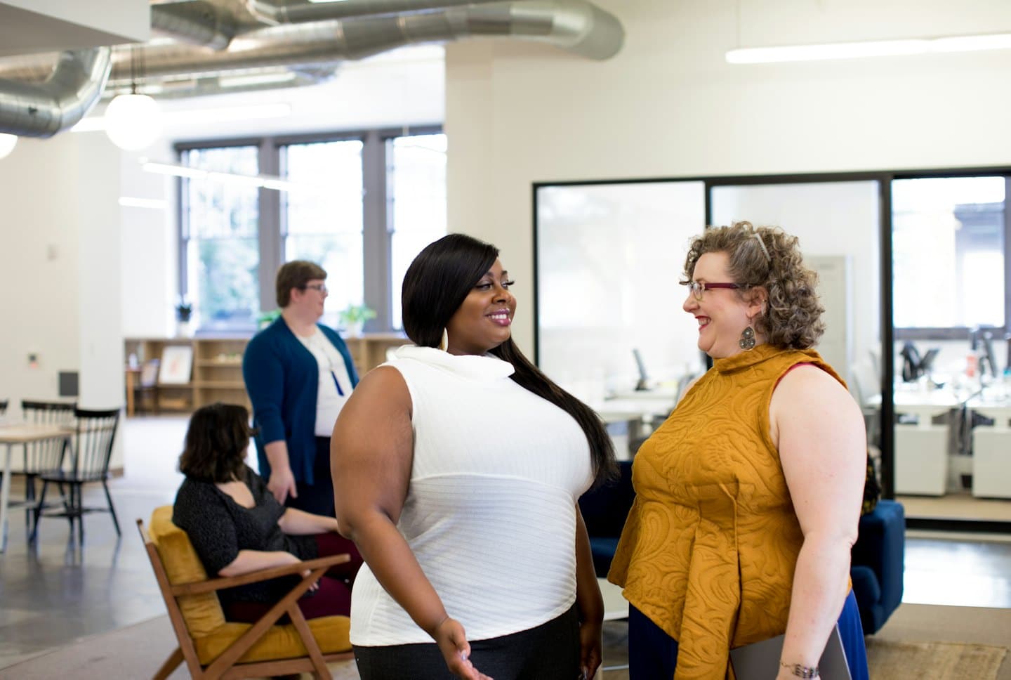 Two women smiling and talking in a modern office.